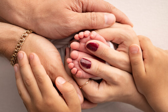 The palms of the parents, the eldest child holds the feet of the newborn child. The newborn's legs are in the hands of the mother's father and older brother and sister. Macro photo of foot, heels toes