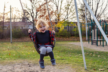 Smiling happy girl on swing in park in autumn. Girl at playground in fall season.