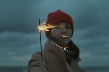 Closeup of firework sparkle stick and blurred woman on backround. Woman wearing warm outwear and...