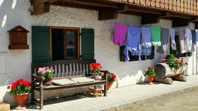 romantischer Hauseingang in Unterammergau mit Holzbank, roten Blumen und Wäsche beim Trocknen