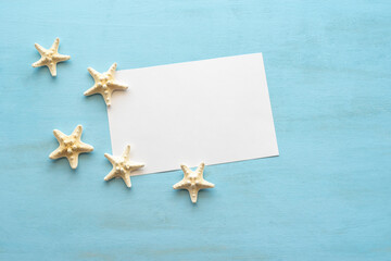 Fototapeta na wymiar Starfishes and empty notebook paper on blue wooden background.