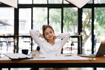 Happy young asian businesswoman relaxing with hands behind head at office desk. Daydreaming concept