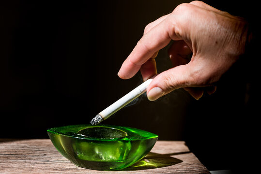 Adult Female Hand Flicking Cigarette Ash Into Green Ashtray, Black Background