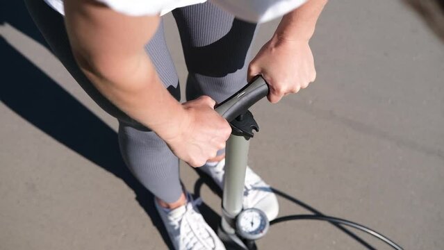close up of hands of woman while inflating and pumping a tire with a hand pump with a pressure gauge manometer outdoors