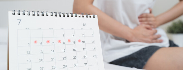 Monthly menstruation symptom period concept. Close up calendar marking on menstruation period day and woman have stomach pain as background. - obrazy, fototapety, plakaty