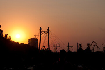 Urban landscape of electricity pylon structure and construction crane silhouettes at sunset