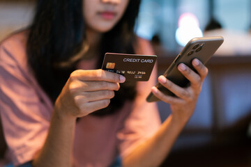 Close-up or closeup of young woman's hand is holding credit card and using smartphone to shop product online at coffee shop. Female shopper flip her credit card to make purchase online transactions.