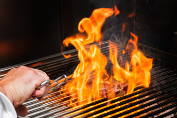 Veal cutlet on the grill with flames of fire and hand with tongs