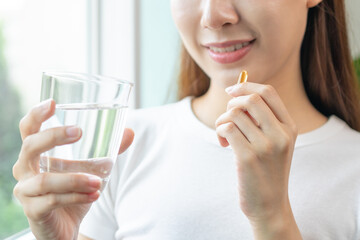 Dietary Supplement, Nutrition asian woman, young hand in holding yellow pill, talking daily vitamin D, E, A, fish oil pill for hair and skin with glass of water. Diet healthy eating, beauty people.