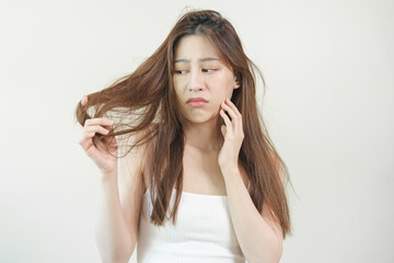 Fototapeta premium Damaged Hair, frustrated asian young woman, girl hand in holding splitting ends, messy unbrushed dry hair with face shock, long disheveled hair, health care of beauty. Portrait isolated on background.