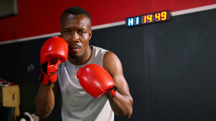 African boxer man in red boxing gloves performing boxing posture and looking at camera with serious...