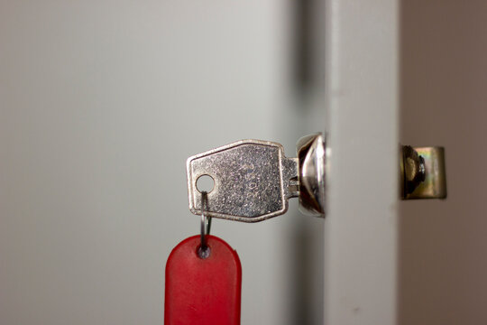 Metal Office Key With Red Fob In Lock Closeup, Horizontal Photo On Blurred Background. Open Door With Key, Safety System For Document Files And Information