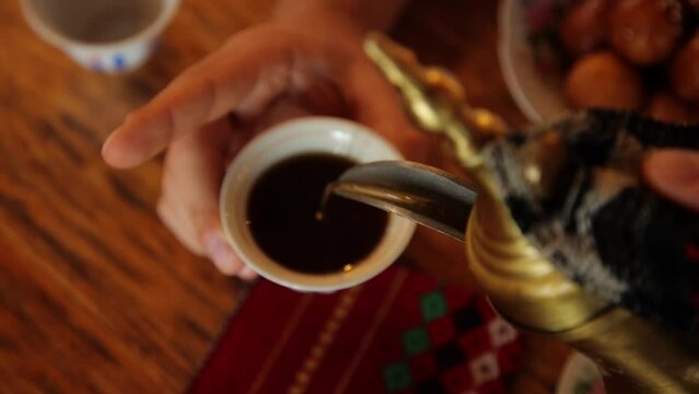 Man's hands pour some tea or coffee from arabic teapot into the cup. High quality FullHD footage