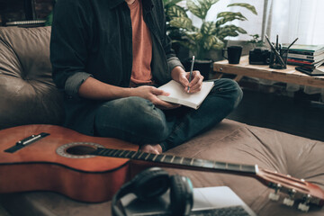 young man relax and playing guitar while sitting on sofa bed in living room at home. Music create melody song, lyrics on laptop and practice concept.
