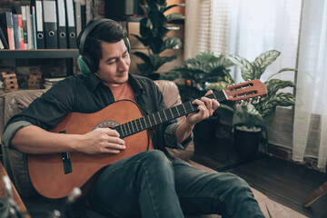 young man relax and playing guitar while sitting on sofa bed in living room at home.