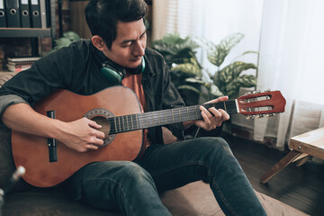 young man relax and playing guitar while sitting on sofa bed in living room at home.