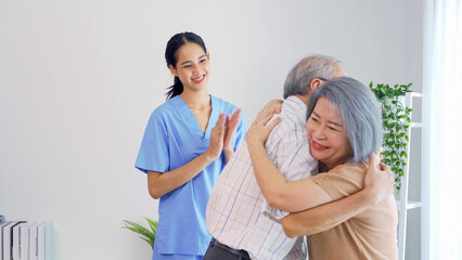 Fototapeta premium Young Asian nurse home care glad to see senior grandparents embracing each other with empathy. Female caregiver is applauding to congratulate the elderly couple family. Life after retirement concept