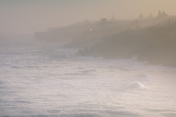 Fototapeta na wymiar Amazing landscape of Atlantic ocean at sunrise. View on morning fog, big waves and stony coast. Beach of Praia das Macas. Colares. Portugal. Concept travel of Europe. 