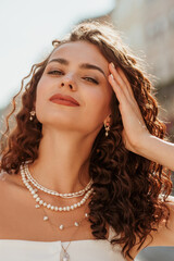 Beautiful happy smiling curly brunette woman wearing trendy pearl layered necklace, posing in...