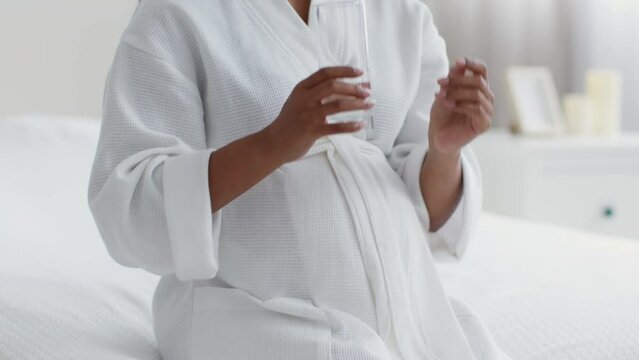 Pregnancy and healthcare. Pregnant black lady drinking vitamins and glass of water, taking supplements, slow motion