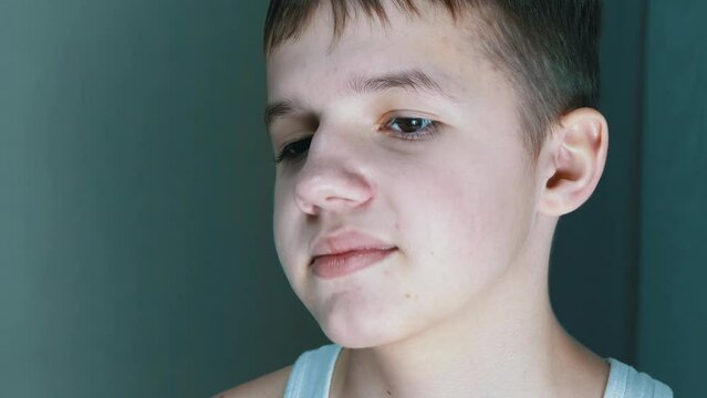 Close-up Face of an Embarrassed Shy Teenager with Downcast, Blinking Eyes. Portrait of a sad handsome serious caucasian boy with long eyelashes, plump lips. A child thinks, ponders, moves eyes, looks
