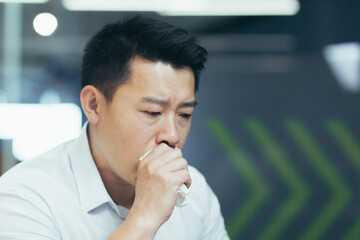 Photo close-up portrait of an Asian man in a shirt, a sick businessman coughs into a tissue.