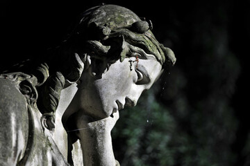 Partial view of an old, weathered sandstone sculpture of a grieving angel on a cemetery in Berlin...