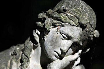 Partial view of an old, weathered sandstone sculpture of a grieving angel on a cemetery in Berlin Germany.	