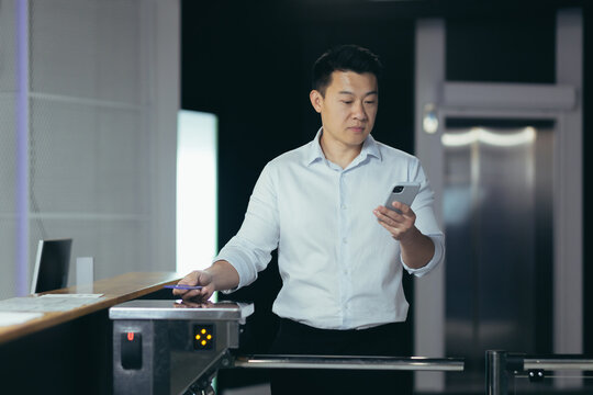 Successful Asian businessman worker enters office, uses key card to open turnstile, man looks at phone screen reads news - Powered by Adobe