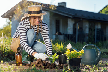 Stylish young woman-gardener planting a plant in garden