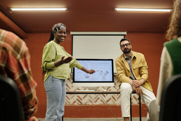Happy young African American speaker pointing at computer screen with diagrams and other financial data while explaining it to colleagues