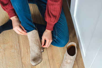 Young woman sitting on the floor, putting on some high heeled suede boots