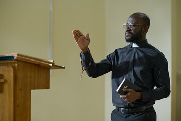 Confident African American man in pastor apparel with clerical collar preaching during church...