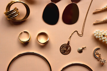 Various gold jewelry and pearl hair clips on peach colored background. Flat lay.