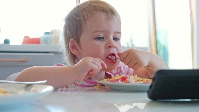 Cute Caucasian Toddler Baby Girl Eating Breakfast and Watching Video on Smartphone