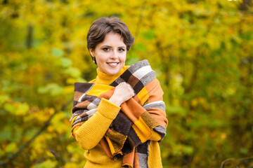 Cheerful smiling young brunette wrapped in blanket in autumn forest