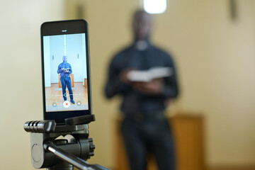 Smartphone with African American pastor in black pants and shirt with clerical collar holding open...