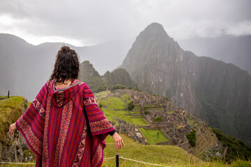 Woman Looking at Inca Citadel called Machupichu built of stones on the mountain, cloudy day, Peru