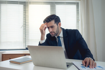 Businessman sits at a desk with a computer holding his head in the stress of working