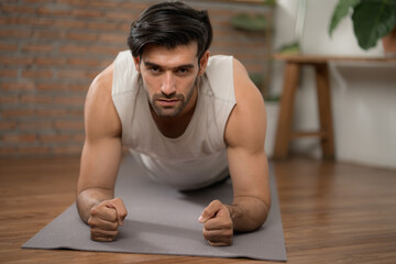 Hansome man with big muscle concentrate on body plank exercise on yoga mat at home gym