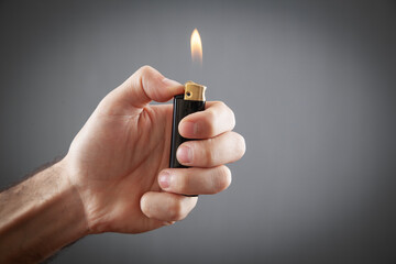 Male hand burning lighter in grey background.