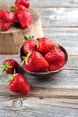 Ripe red strawberries from organic cultivation offered as a close-up in a rustic design bowl on old faded wood