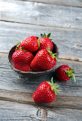 Ripe red strawberries from organic cultivation offered as a close-up in a rustic design bowl on old faded wood