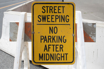 outdoor yellow black metal street sign with a message of street sweeping no parking after midnight...