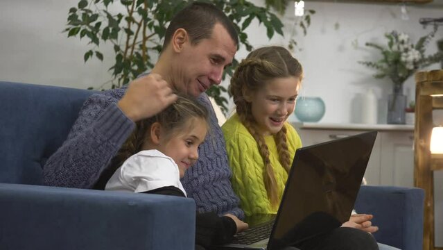 Happy family sitting together at home at computer.coach,children look at laptop screen, smile, enjoy their leisure time shopping online store.Children with coach father use laptop for online education