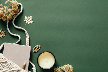Flat lay aesthetic feminine workspace with macrame handbag, candle, dried flowers on green background. Top view cozy home, bohemian woman office desk table. Autumn, fall concept.