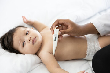 doctor measuring baby's temperature on bedroom