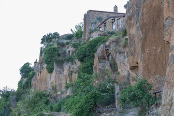 Fototapeta premium Ancient buildings of bricks of stones in sunny summer day on a background of the sky with lots of greenery in a courtyard and partially overgrown walls by climbing plants.