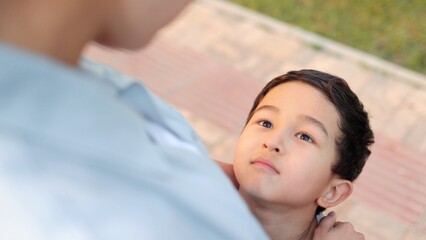 Close up view of son looking at his mom upwards. Mother hugs her son by the shoulders