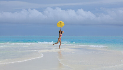 girl in a bikini with a yellow umbrella on the sea sand